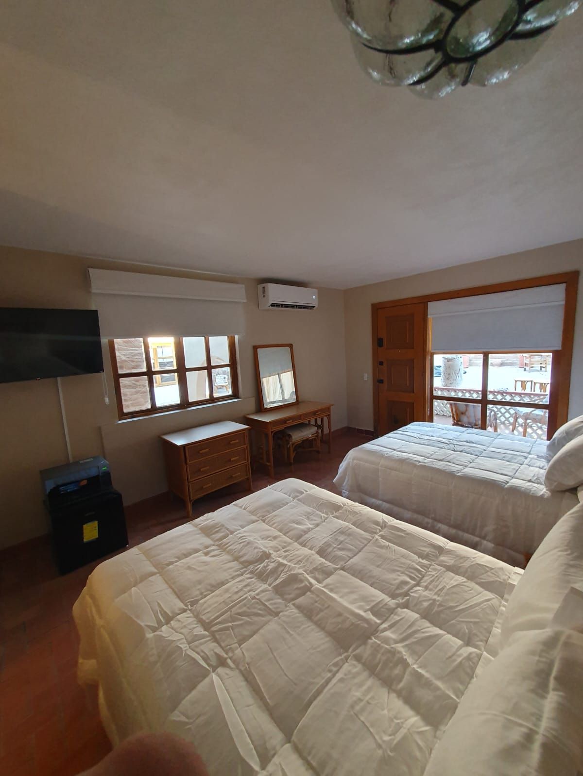 Een slaapkamer met twee bedden, een dressoir, een bureau en een airconditioning.