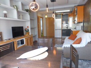 A modern kitchen with a refrigerator, microwave, and sink. There is a dining area with a table and chairs, and a television on a wooden cabinet. - Charming 1-Bedroom Apartment near the beach in Roquetas de Mar, Spain (Roquetas de Mar)