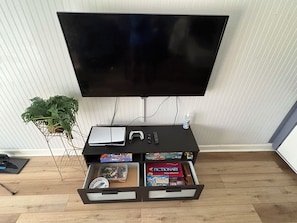 A flat-screen TV mounted on a wall, a gaming console, a remote control, a notebook, and a drawer with board games. - 3 BR Home, Near Bike Trail, Game Room, 20 mins to DFW Airport and AT&T Stadium (Bedford)
