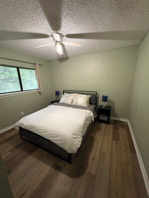 Quarto com cama, mesas de cabeceira, ventoinha no teto e janela.