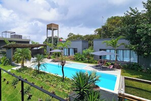 A modern outdoor pool area with a clear blue pool, surrounded by lush greenery and a few lounge chairs.