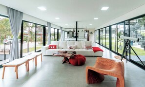 A spacious living area with a white sofa, red cushions, a wooden coffee table, and a telescope on a tripod.