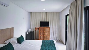 A hotel room with a bed, a television on a wooden stand, and a window with curtains. - Celia’s Beautiful House (Tibau do Sul)