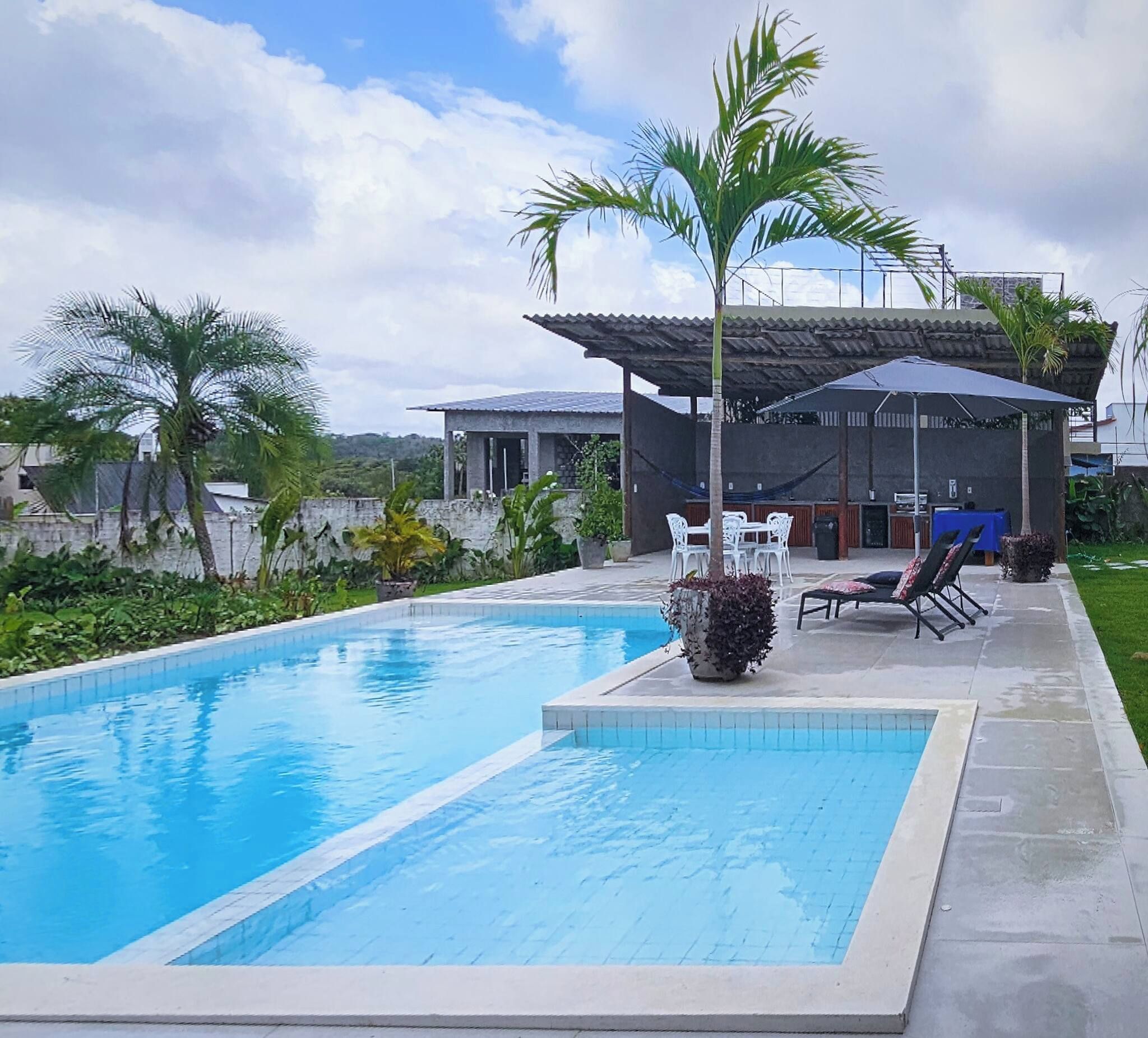 Une piscine dotée d’une terrasse carrelée, de chaises longues et d’un espace extérieur aménagé et abrité.