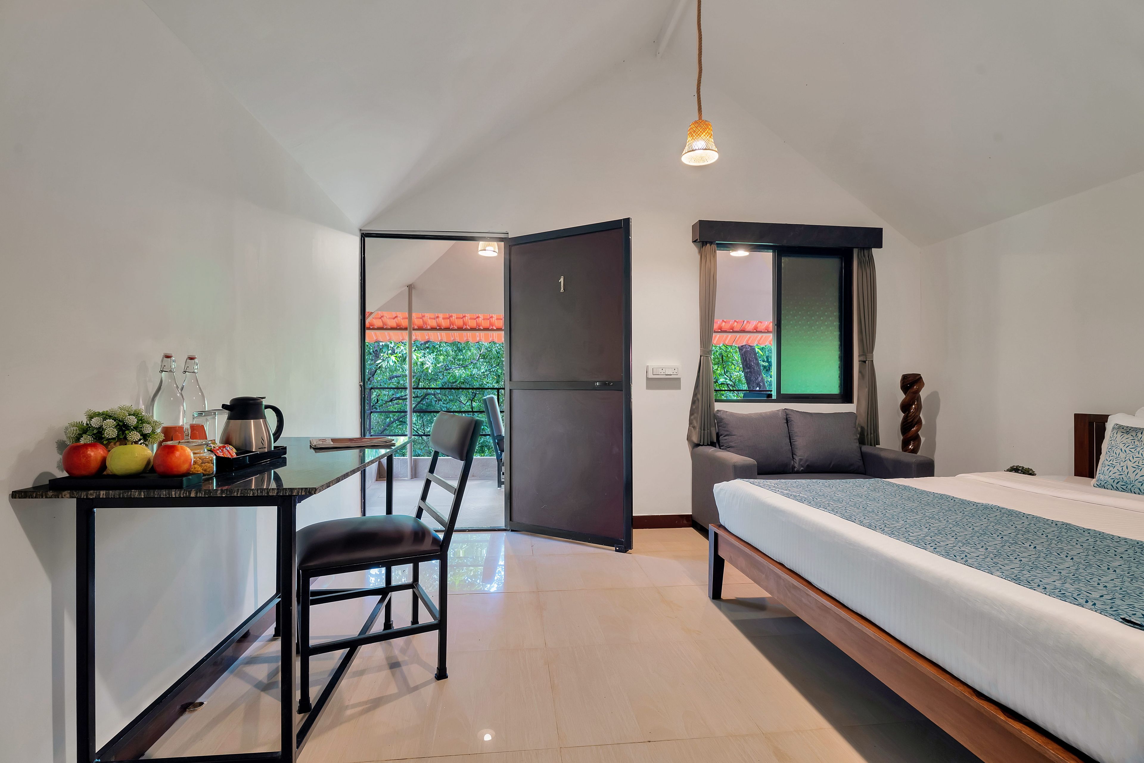 A modern bedroom with a bed, a desk with a chair, and a view of greenery outside.