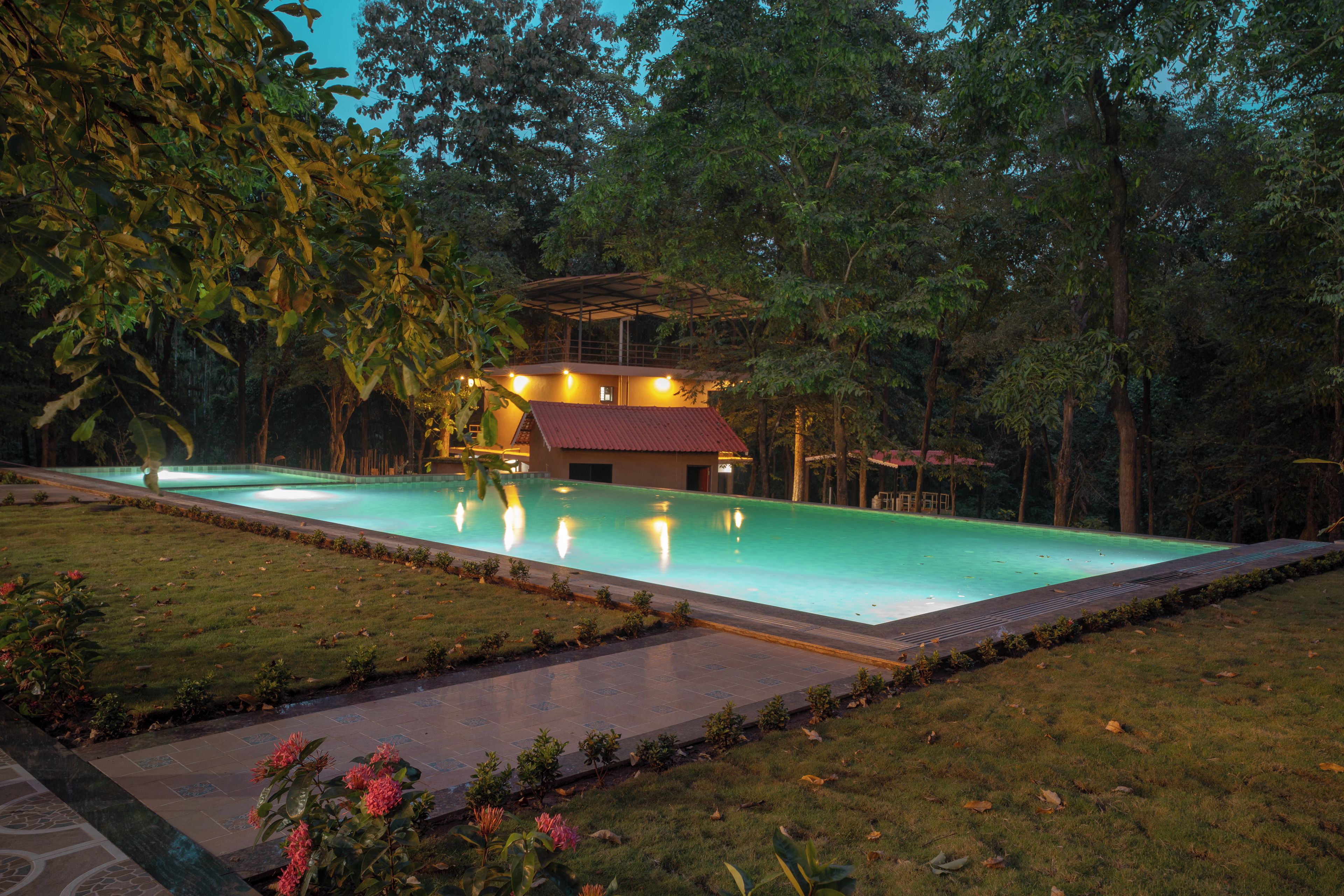 Piscina com jardim ao redor e um edifício com telhado vermelho.