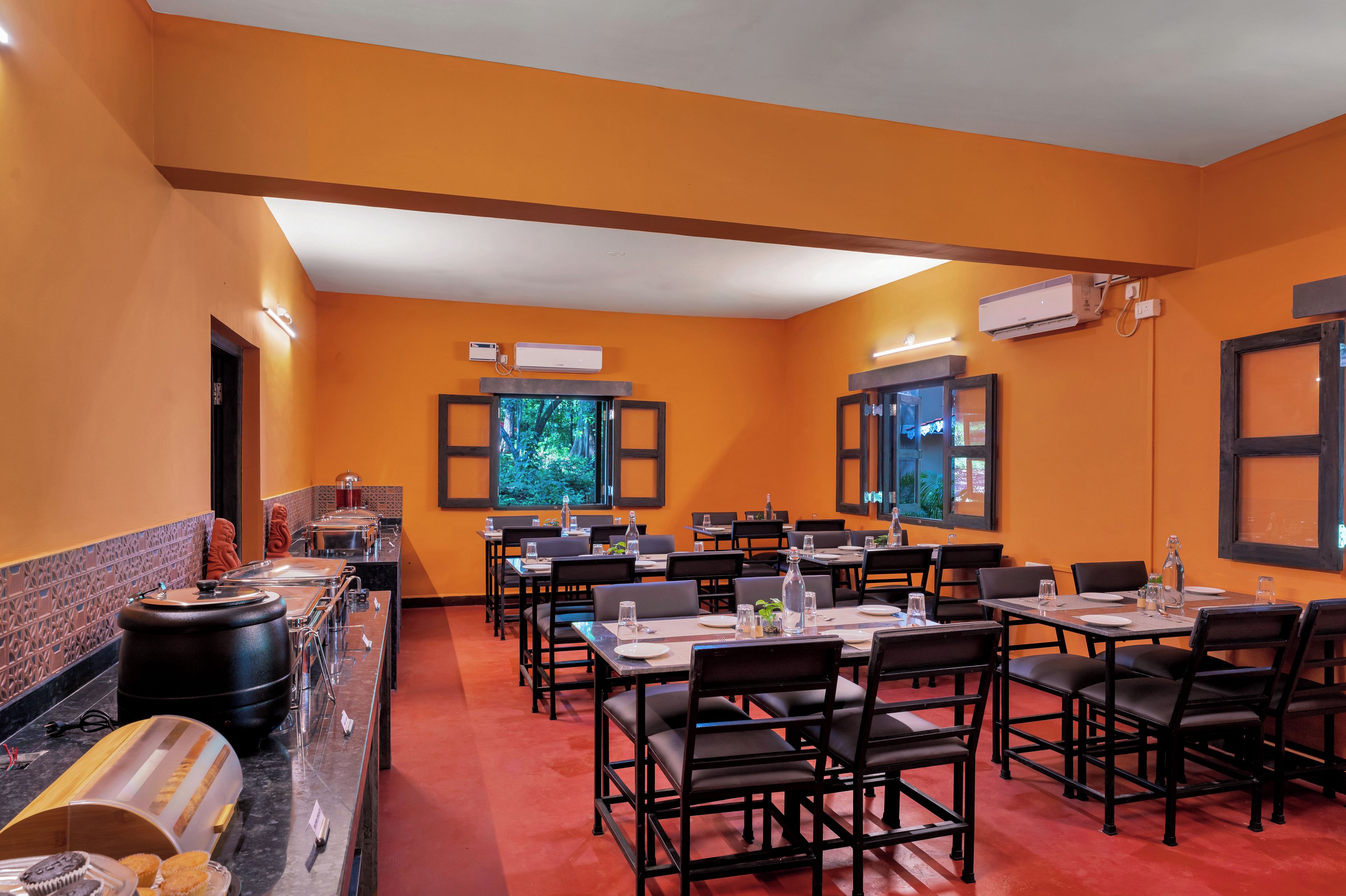 Un restaurante con paredes naranja, sillas negras y una zona de bufé con recipientes de comida.