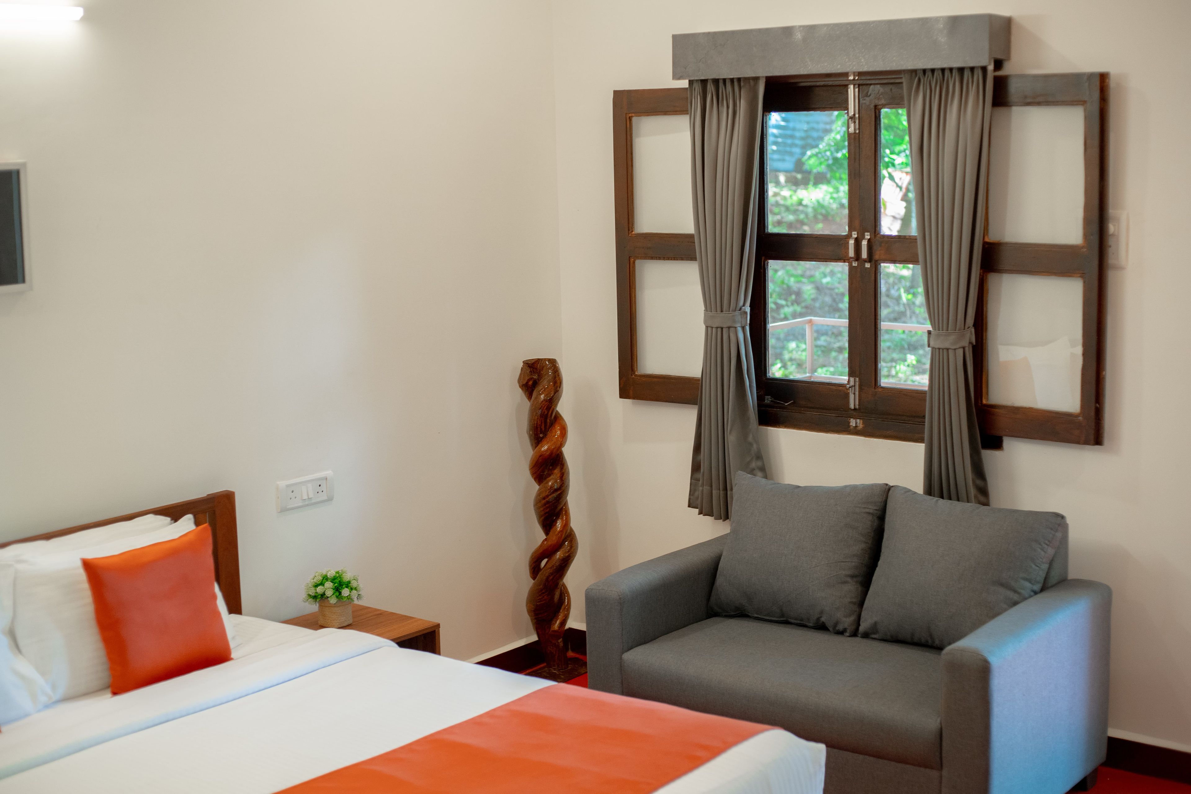 Habitación de hotel con una cama, un sillón gris, una ventana con cortinas y un televisor montado en la pared.
