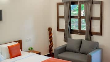 Habitación de hotel con una cama, un sillón gris, una ventana con cortinas y un televisor montado en la pared.