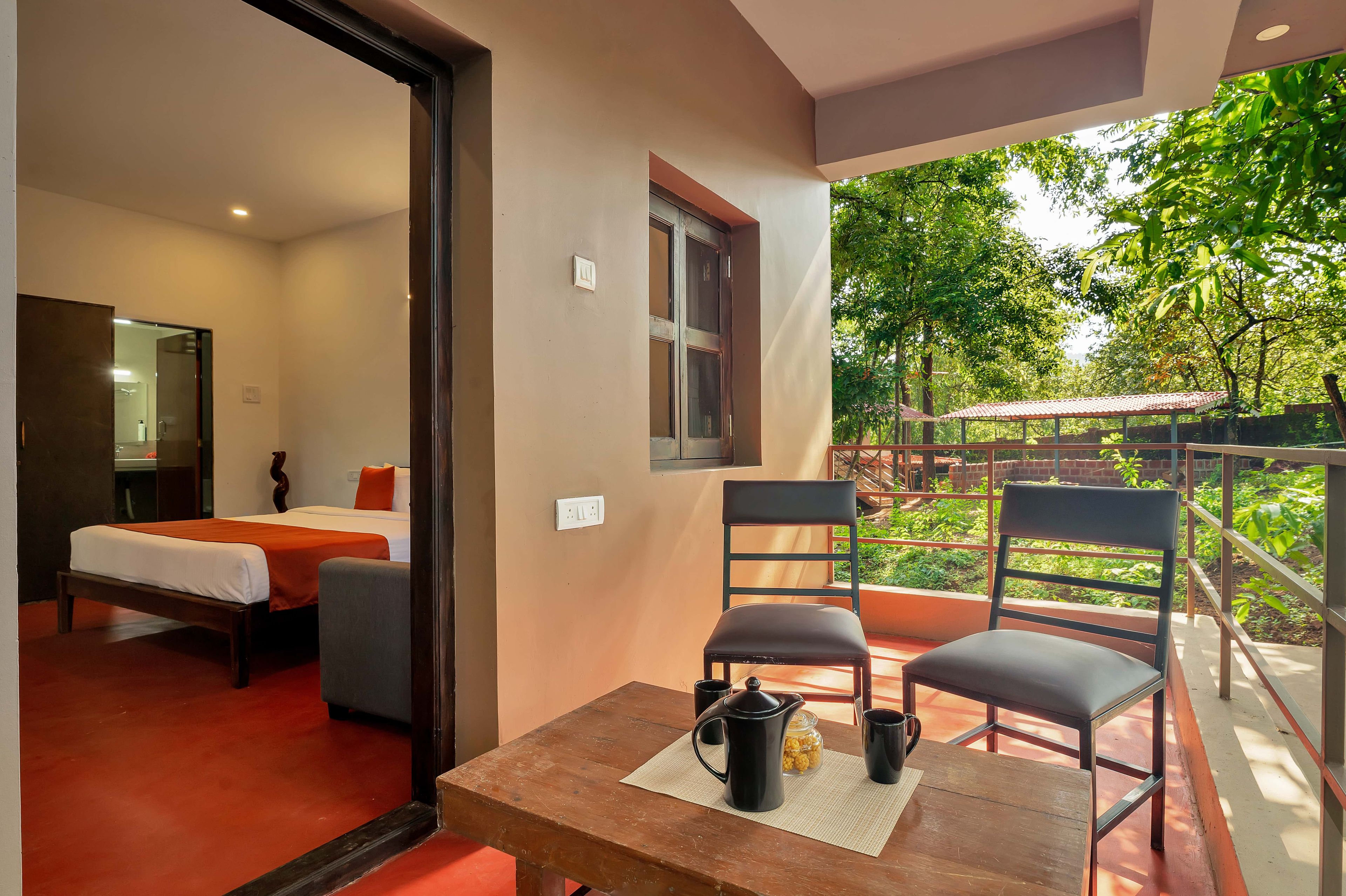 A hotel room with a balcony, a bed, a table with a coffee pot, and chairs.