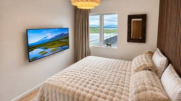 A bedroom with a large bed, a television mounted on the wall, a window with a view of a landscape, and a wooden headboard.