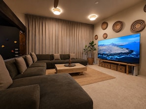 A modern living room with a sectional sofa, a coffee table, a large flat-screen TV, and a climbing wall.