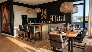 A modern kitchen with a central island, dining area with a wooden table and chairs, and large windows offering a view.