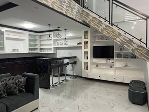 A modern kitchen with a marble countertop, white cabinetry, and a built-in TV.