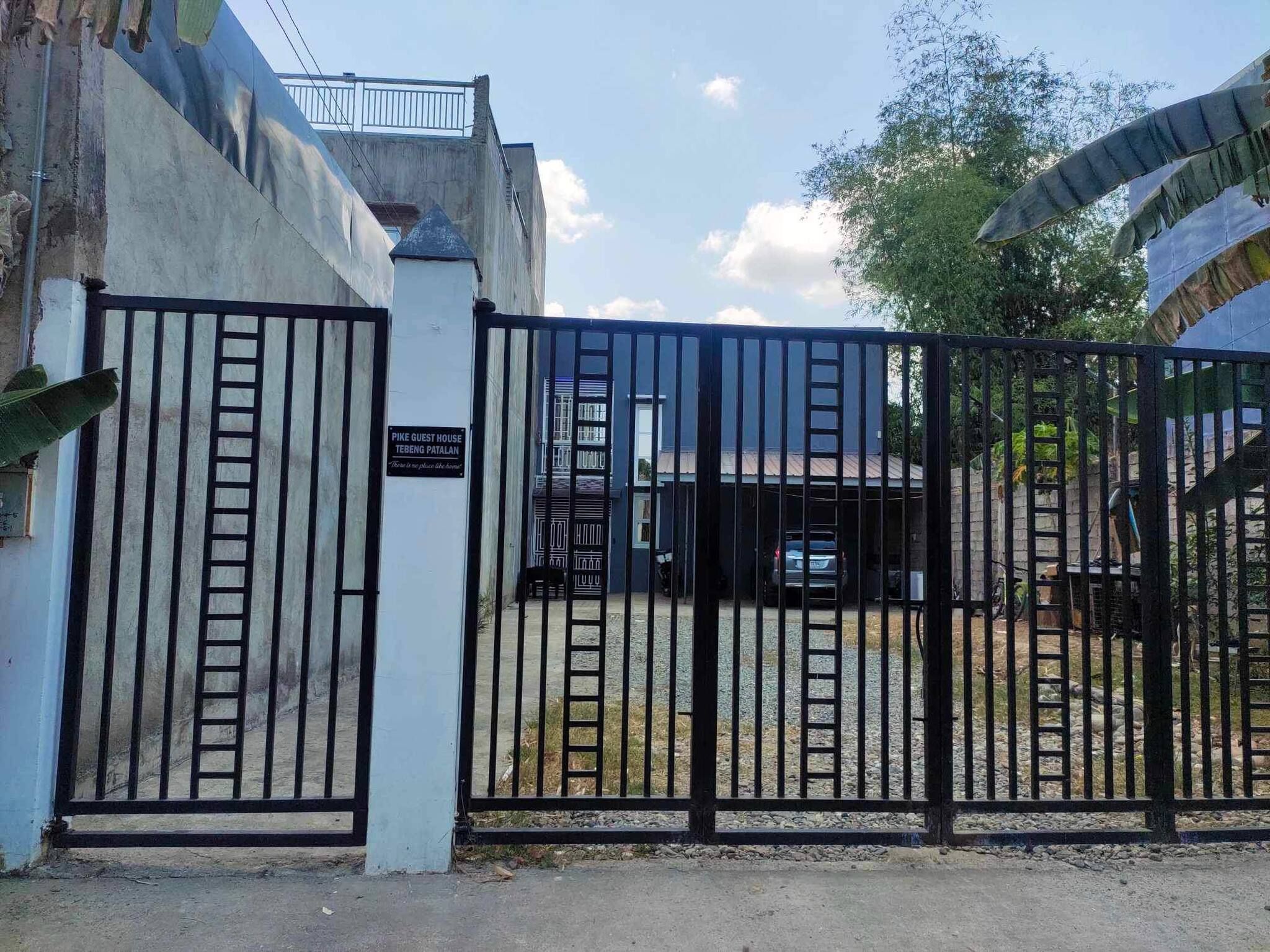 A gated entrance to a property with a sign indicating 'PIKE GUEST HOUSE' and 'TEBENG PATALAN'.