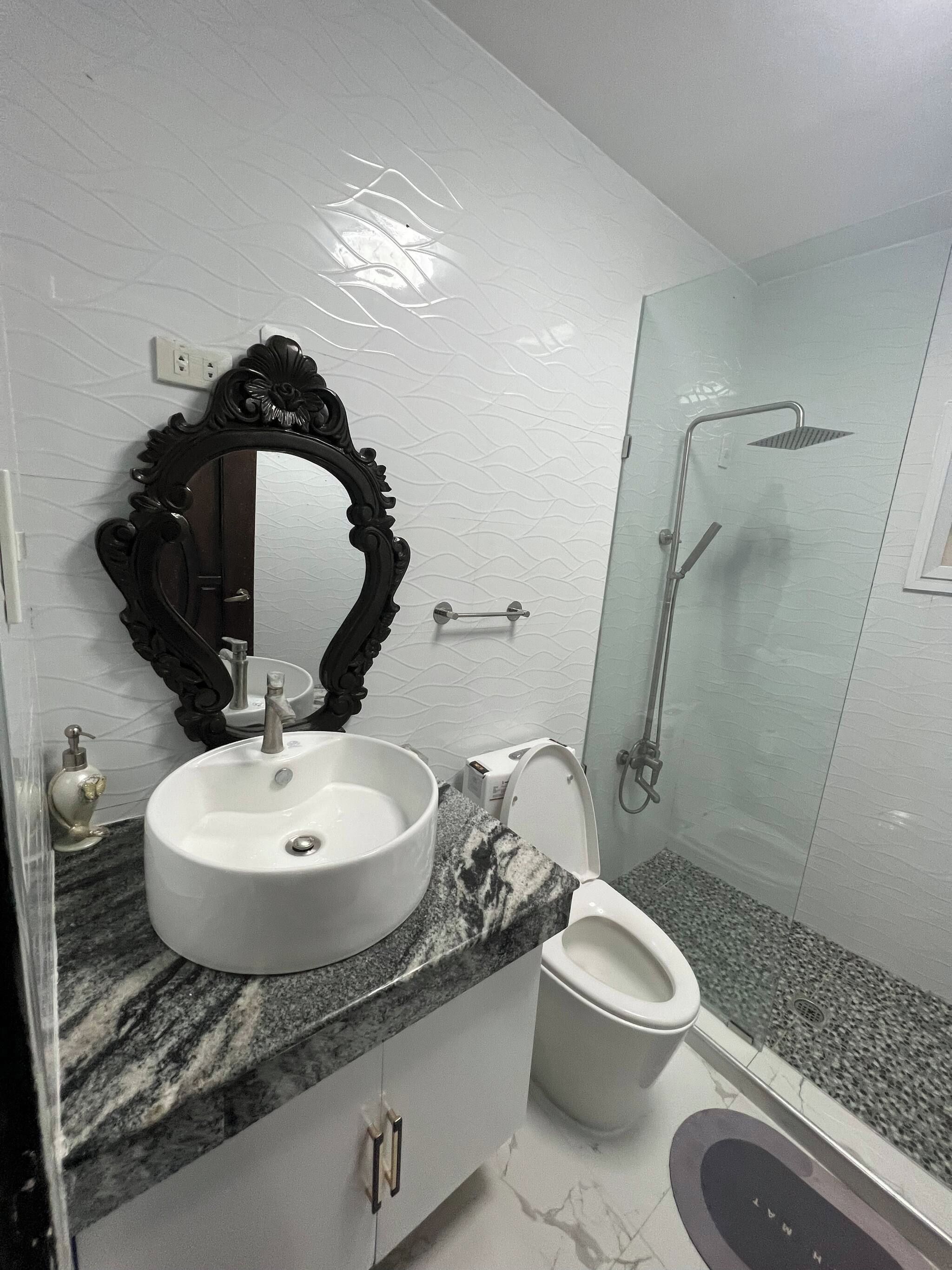 Une salle de bain avec un lavabo en marbre, des toilettes, une douche et un miroir décoratif.