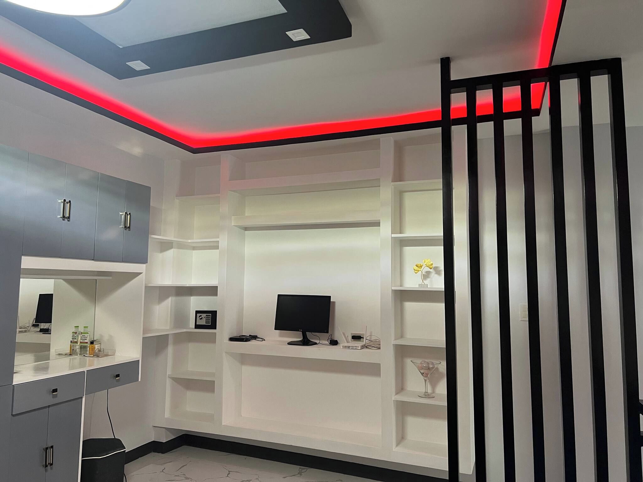 Un dormitorio moderno con televisor empotrado, estanterías y espejo.