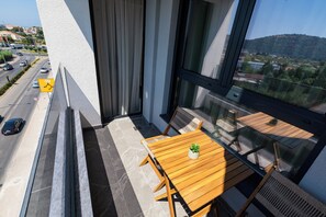 A balcony with a wooden table and chairs, a potted plant, and a view of a road with cars. - One Bedroom Apartment with City View (Bar)