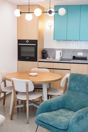 A modern kitchen with a round wooden table, chairs, and a blue armchair. - One Bedroom Apartment with City View (Bar)