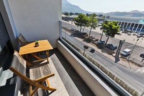 En balkon med et træbord og stole, med udsigt over en parkeringsplads og en bygning med skiltet 'HDL MARKET'.