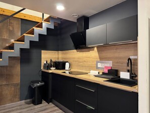 Une cuisine compacte avec un escalier en bois, des meubles noirs et une petite poubelle.