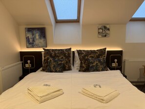 A bedroom with a skylight, two nightstands, a bed with a white duvet, and two towels on the bed. - Charming 2-bedroom Apartment in Heart of Prague (Prague)
