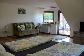 A room with a sofa, a bed with a patterned bedspread, a radiator, and a window with curtains. - Holiday apartment with 1 bedroom (Gössweinstein)
