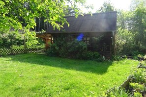 A wooden structure with a metal roof, surrounded by a well-maintained grassy area and dense foliage. - Holiday apartment with 1 bedroom (Gössweinstein)