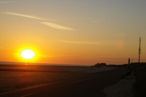 A sunset over a beach with a road and a lighthouse in the distance. - Holiday apartment with 1 bedroom (Borkum)