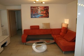 Ein Wohnzimmer mit einem roten Sofa, einem Glastisch und einem Bild an der Wand.