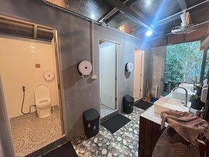 Et badeværelse med toilet, bidet og håndvask. Der er en skraldespand og et håndklædetørrestativ. Gulvet er belagt med et mønstret flisemønster.