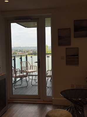 Ein Zimmer mit einer Schiebetür zu einem Balkon im Freien und Blick auf eine Stadtlandschaft.