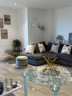 Ein modernes Wohnzimmer mit einem Ecksofa, einem Glastisch und einem runden Teppich.