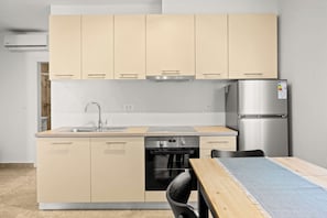 Een compacte keuken met beige kastjes, een roestvrijstalen koelkast en een inbouwoven.