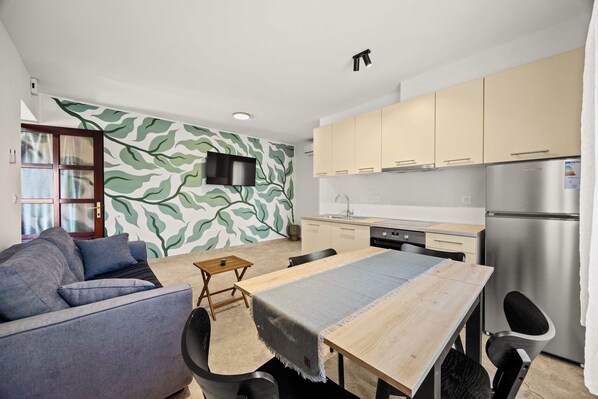 Eine moderne Küche mit Einbauofen, einem Esstisch mit Stühlen und einer Wohnbereich mit Sofa und Wand-Fernseher.