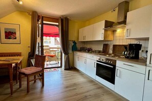A compact kitchen with white cabinets, a stove, and a dining area with a wooden table and chair. - Apple blossom at the Bayer house (Pottenstein)