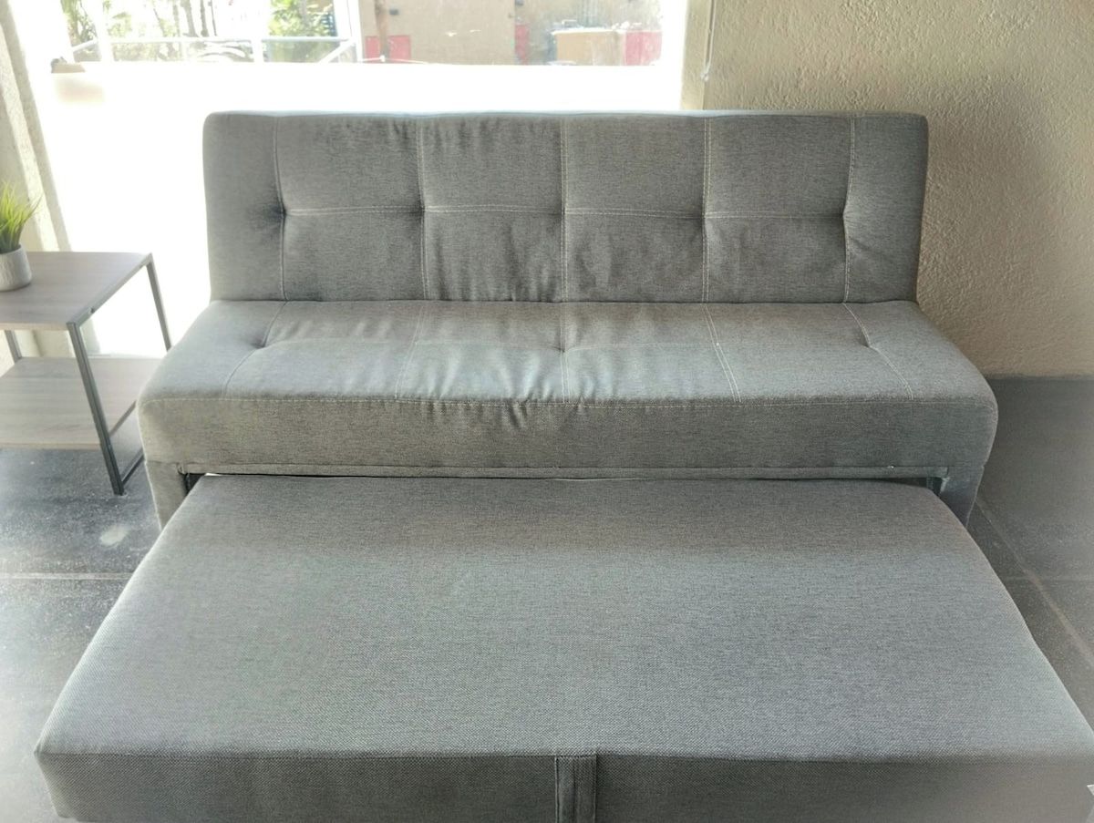 Un canapé gris accompagné d’un pouf assorti, dans une pièce dont le sol est recouvert de carreaux et où se trouve une petite table sur laquelle est posée une plante.