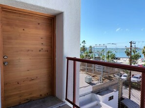 A wooden door with a metal gate, a balcony with a view of a parking area and palm trees. - Suites Buenavista 301 y 302 (La Paz)