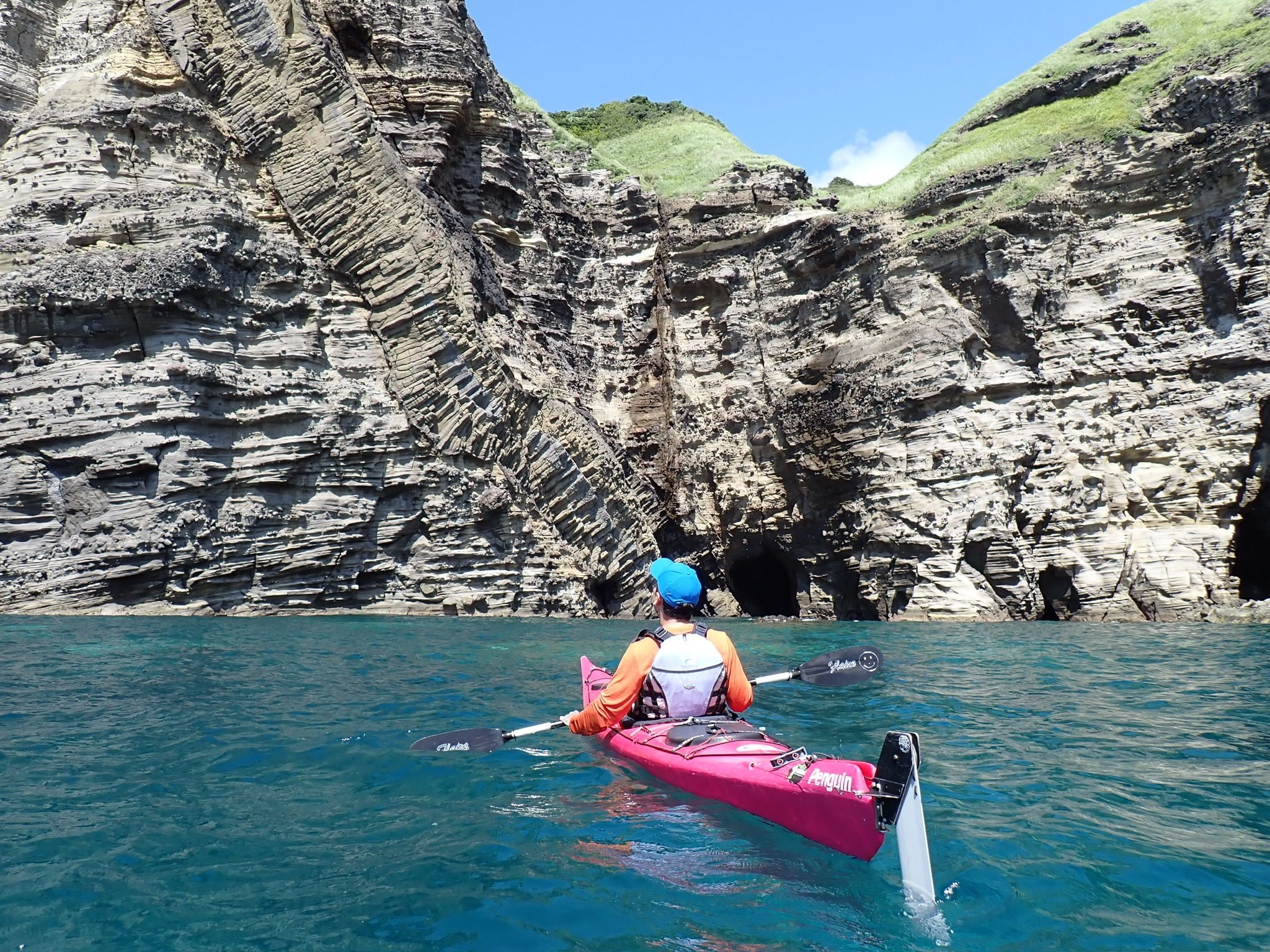 Un kayakista en un kayak rosa sobre aguas tranquilas, con acantilados rocosos al fondo.