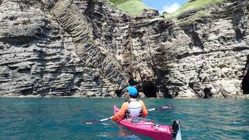 Un kayakista en un kayak rosa sobre aguas tranquilas, con acantilados rocosos al fondo.