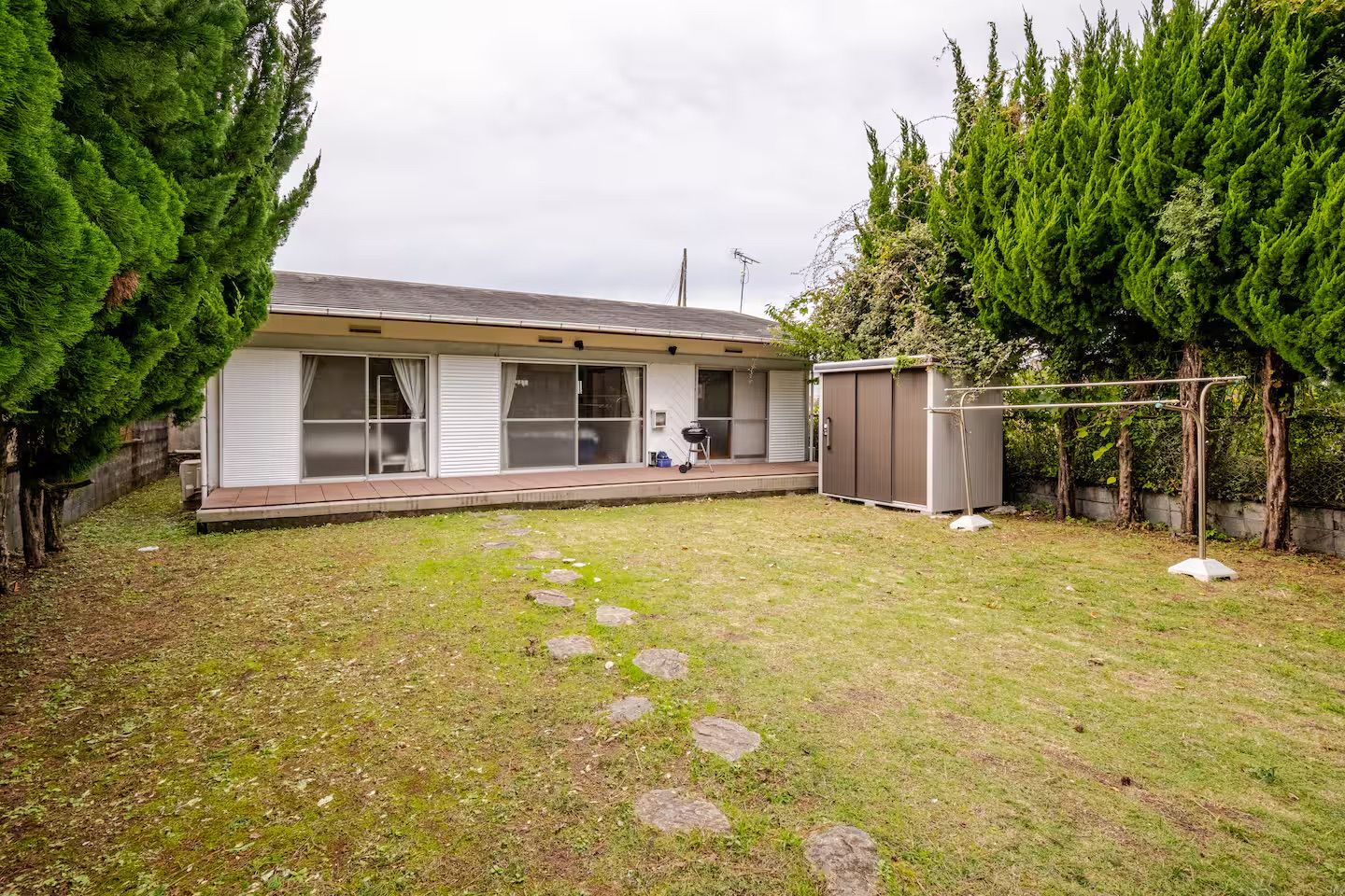 A residential property with a house, a covered patio, a fenced yard, and a small shed.