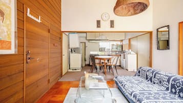 A compact living space with a wooden door, a dining area with a table and chairs, a sofa with patterned cushions, and a kitchen area with appliances.