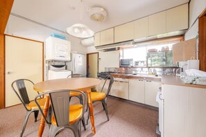 A compact kitchen with a dining table, chairs, a refrigerator, a stove, and a microwave. - KIKA STAY (Minamiizu)