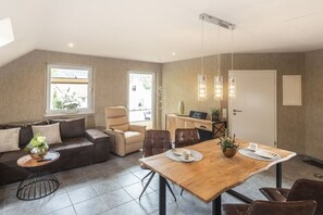 A modern living room with a sofa, armchairs, a dining table, and a kitchen area. - Holiday apartment with 1 bedroom (Steinbach-Hallenberg)