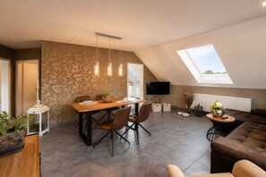 A modern living space with a dining area, a sofa, a TV mounted on the wall, and a skylight. - Holiday apartment with 1 bedroom (Steinbach-Hallenberg)