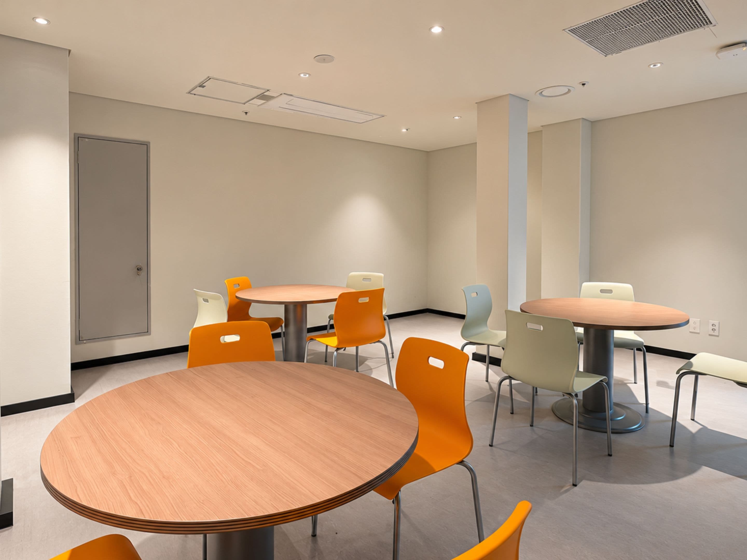 A conference room with round tables and chairs, a door, and a ceiling with recessed lighting.