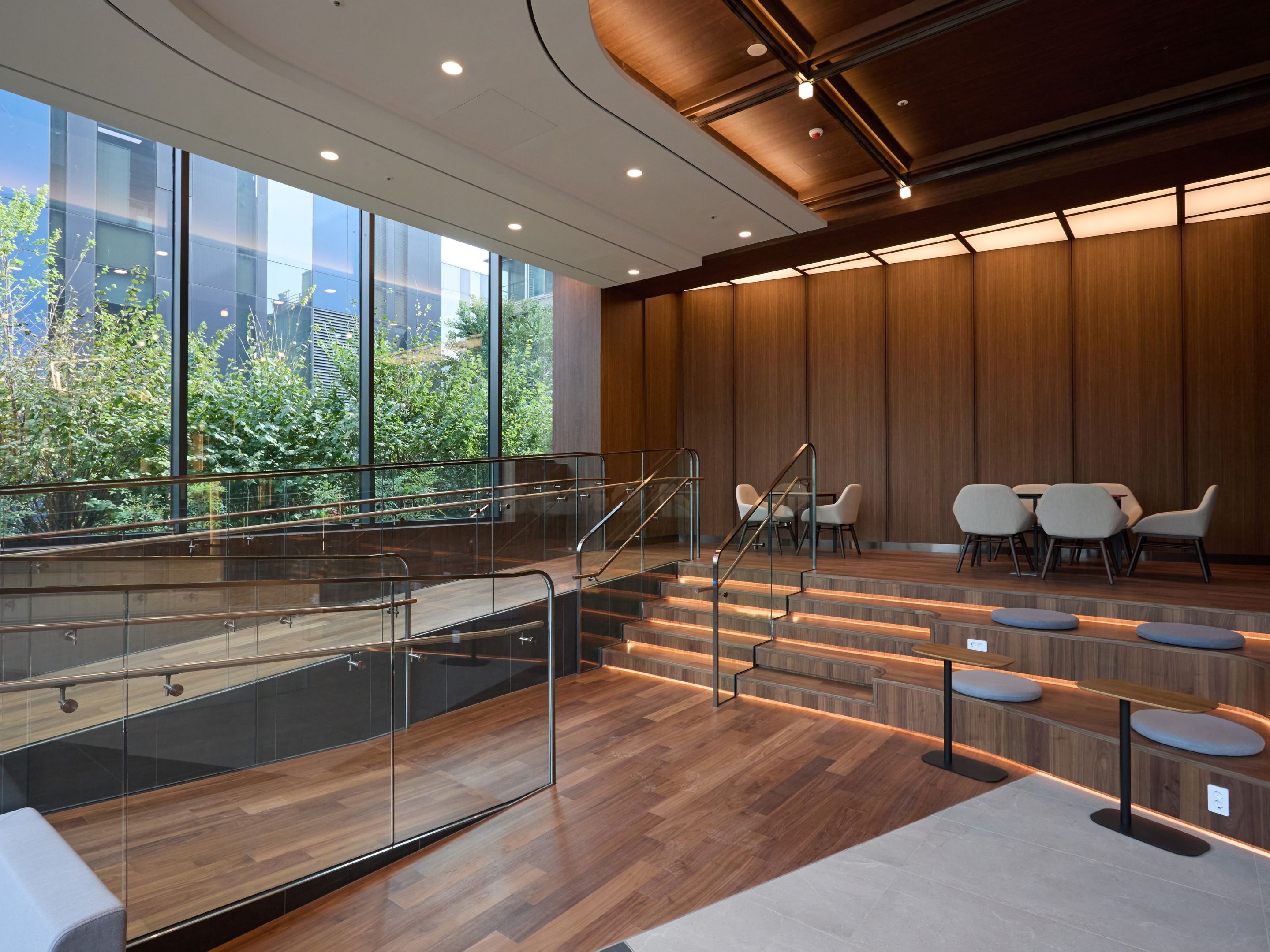 A modern interior with a glass staircase, wooden panel walls, and seating areas.