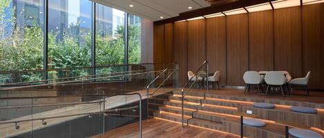 A modern interior with a glass staircase, wooden panel walls, and seating areas.