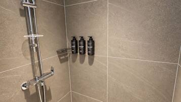 A shower area with a chrome showerhead, a handheld shower attachment, and four bottles of shampoo and conditioner on the wall.