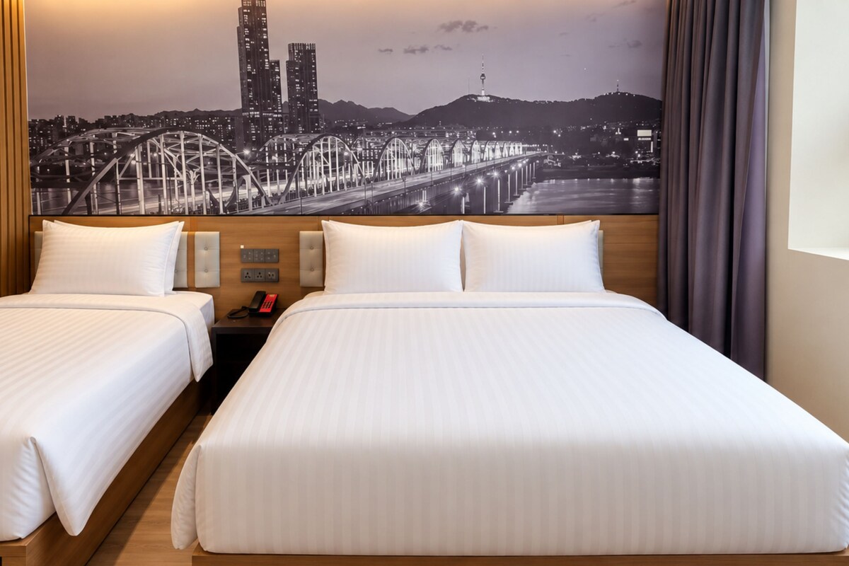 A hotel room with two beds, a cityscape view, a wooden headboard, and a nightstand with a phone.
